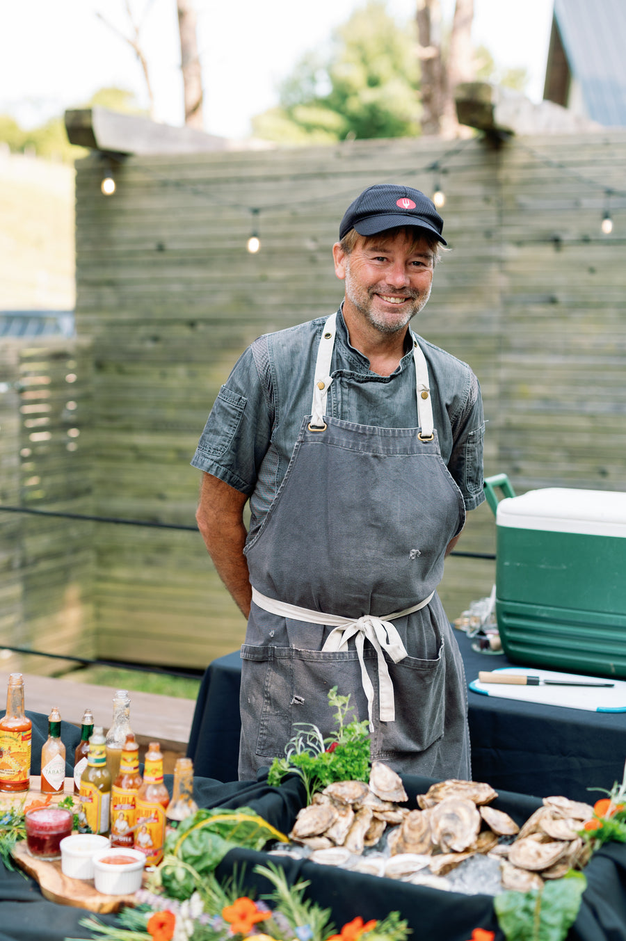 Man in apron standing behind a table with fresh seafood and drinks outdoors